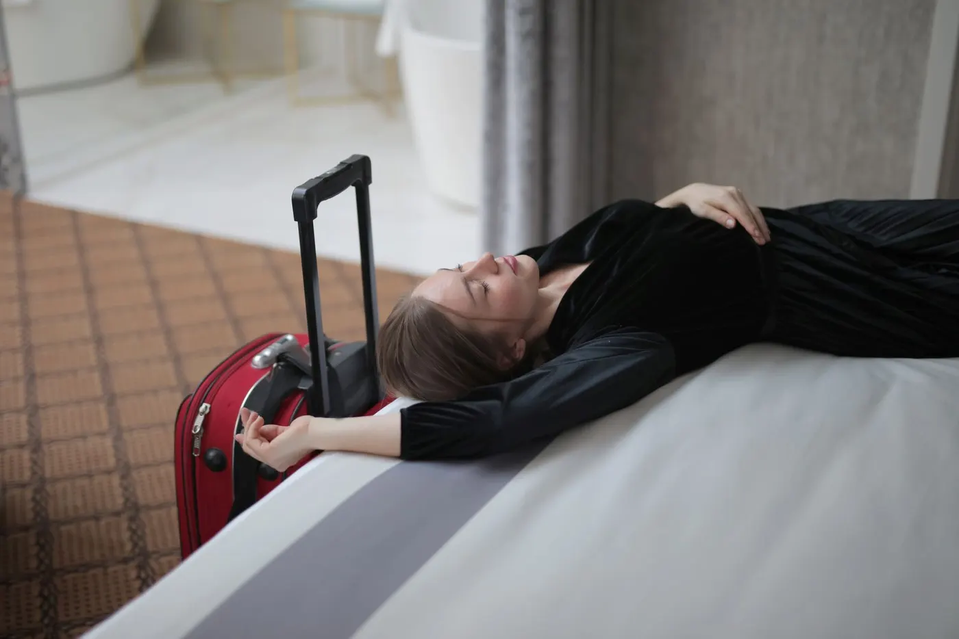 Une voyageuse épuisée se repose sur un lit d'hôtel, à côté de sa valise