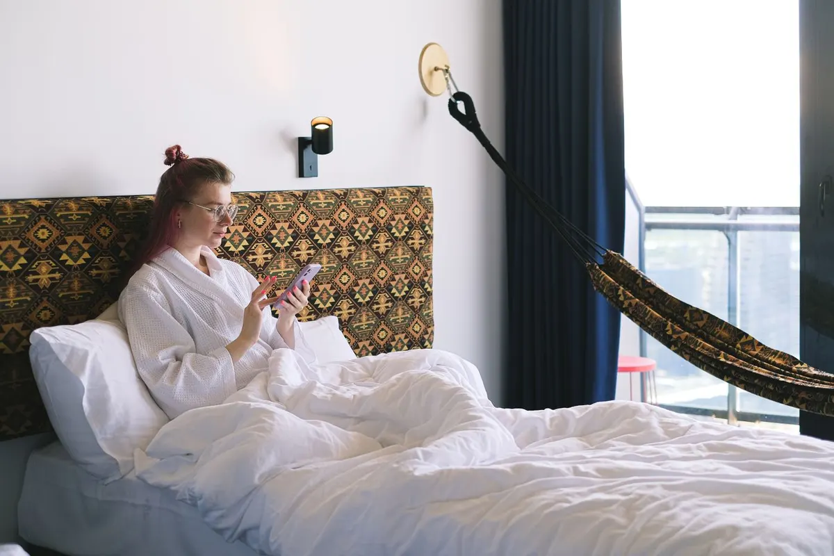 Une voyageuse consulte son téléphone depuis un lit d'hôtel