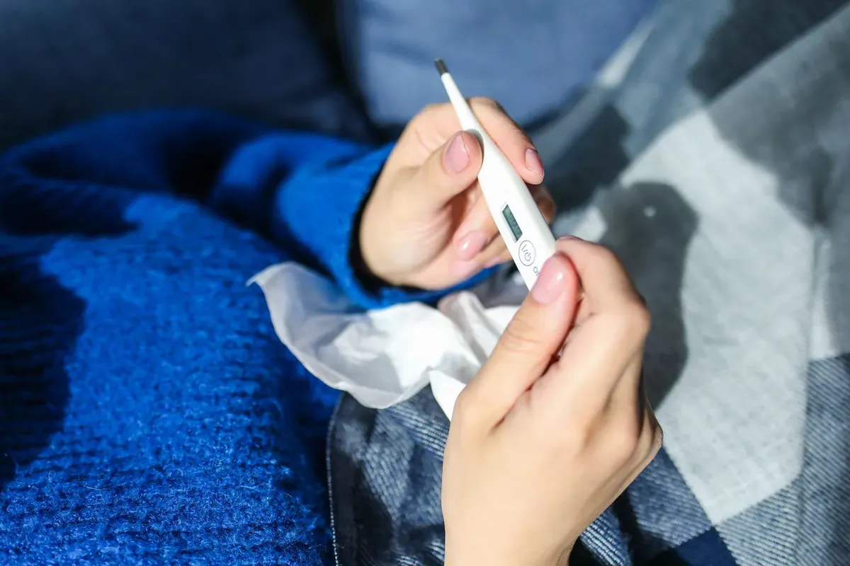 Une personne tenant un thermomètre, allongée sous une couverture